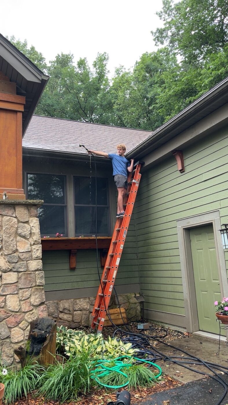Technician on a ladder clearing and cleaning an exterior gutter